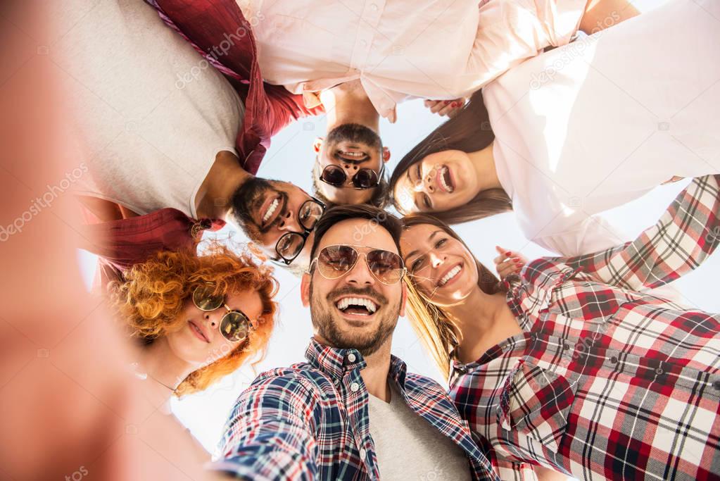 Group of young people standing in a circle, outdoors, making a selfie