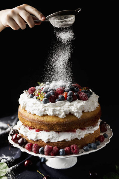 Шеф-повар готовит красивый фруктовый торт с ингредиентами для приготовления пищи на темной скатерти
