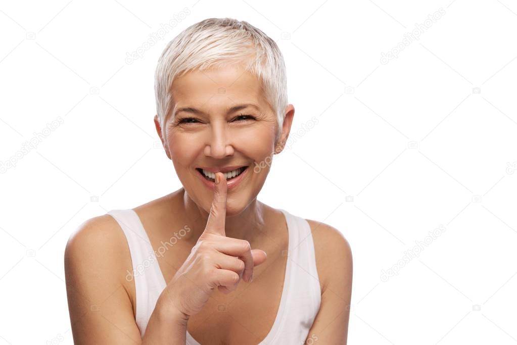 Portrait of a beautiful elderly woman showing silence gesture, smiling, isolated on white background