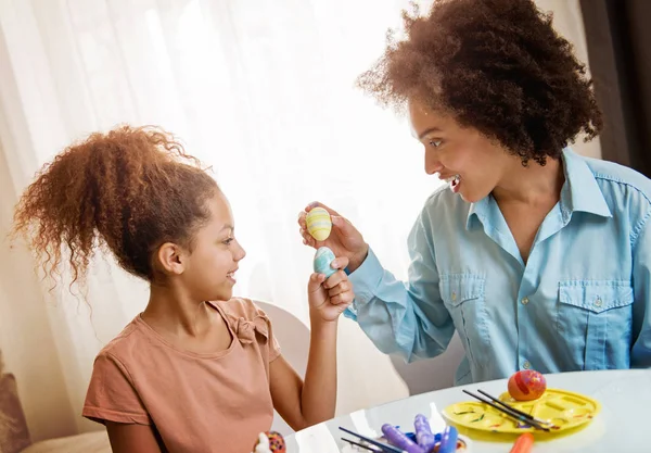 美しいアフリカ系アメリカ人の女性と彼女の娘がテーブルでイースターの卵を着色 — ストック写真