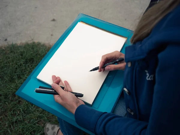 Young female draws on paper with felt pen.