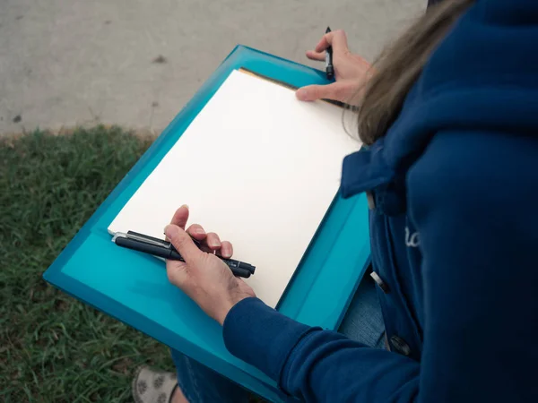 Young female draws on paper with felt pen.