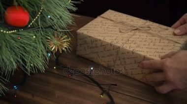 Adam hediye kutuları Noel ağacının altına koyar. Köknar ahşap masa standı ve parlayan garland ve Noel oyuncaklar ile dekore edilmiş.