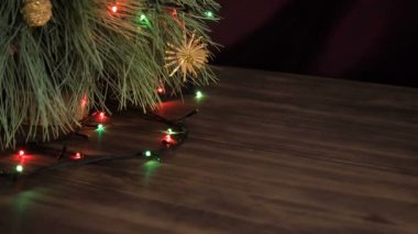 Adam hediye kutuları Noel ağacının altına koyar. Köknar ahşap masa standı ve parlayan garland ve Noel oyuncaklar ile dekore edilmiş.