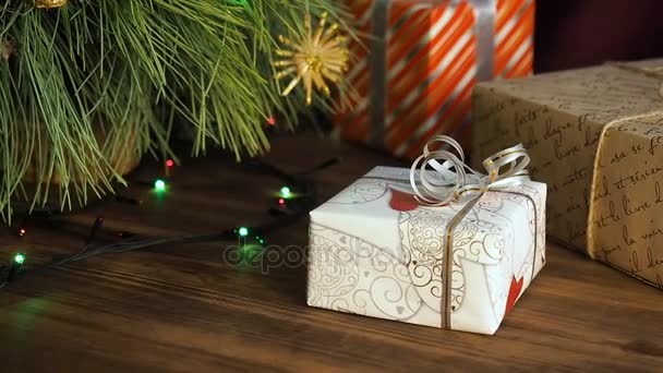 Hay cajas de regalos debajo del árbol. Los regalos están llenos de papel colorido y atados con cuerdas y cintas. Guirnalda de Navidad en las ramas de abeto. Ramas de árboles de cerca, movimiento de desplazamiento, panorama — Vídeos de Stock