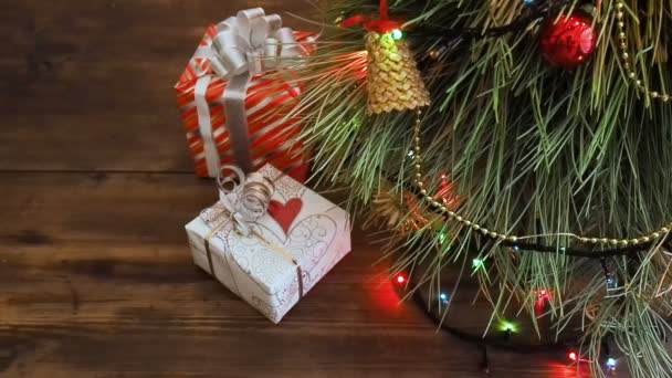 Hay cajas de regalos debajo del árbol. Los regalos están llenos de papel colorido y atados con cuerdas y cintas. Guirnalda de Navidad en las ramas de abeto. Ramas de árboles de cerca, movimiento de desplazamiento, panorama — Vídeos de Stock