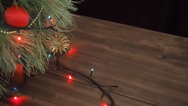 Człowiek stawia paczek z prezentami pod choinkę. Jodła stanąć na drewnianym stole i ozdobione świecącą garland i Boże Narodzenie zabawki. — Wideo stockowe