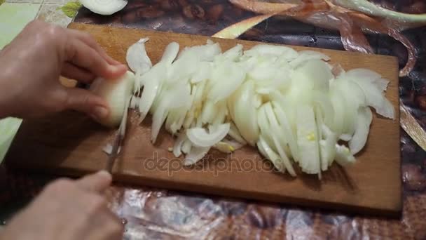 Jovem na cozinha cortando as cebolas com faca na tábua de corte de madeira — Vídeo de Stock