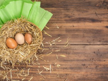 Kahverengi yumurta saman içinde iç içe. Kırsal çevre kahverengi tavuk yumurtası ve saman eski ahşap plakalar arka plan üzerinde arka plan. Üstten Görünüm. Paskalya kartları veya Restoran Menü yaratıcı arka plan