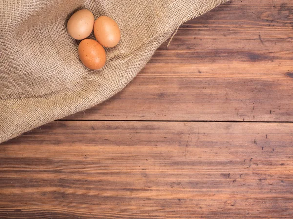 Huevos de pollo en viejas mesas rurales de madera y fondo vintage de arpillera, vista superior de la foto. Textura Hessiana con huevos sobre fondo de madera para el diseño de la tarjeta de felicitaciones de Pascua o anuncio — Foto de Stock