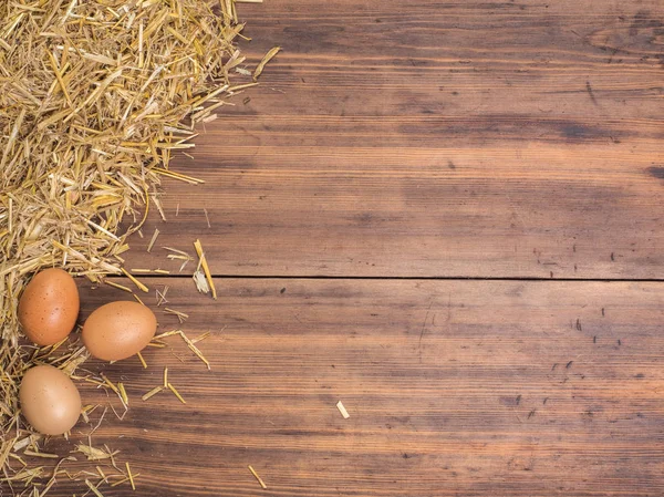 Fondo ecológico rural con huevos de pollo marrón y paja sobre el fondo de tablones de madera viejos. La vista desde arriba. Fondo creativo para tarjetas de Pascua — Foto de Stock