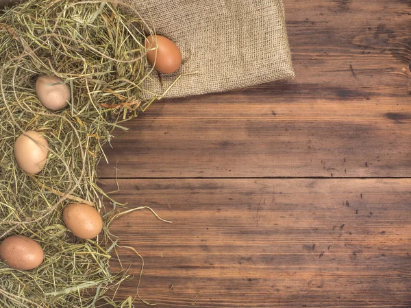 Fondo ecológico rural con huevos de pollo marrón, una pieza de arpillera y paja en el fondo de tablones de madera viejos. La vista desde arriba. Fondo creativo para tarjetas de Pascua — Foto de Stock