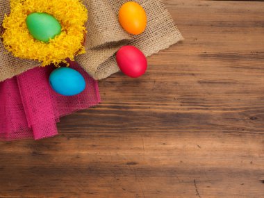 Parlak sarı saman, çuval bezi ve eski ahşap masa arka plan üzerinde renkli tavuk yumurta. Üstten Görünüm.