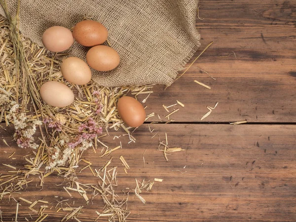 Fondo ecológico rural con huevos de pollo marrón, una pieza de arpillera y paja en el fondo de tablones de madera viejos. La vista desde arriba. Fondo creativo para tarjetas de Pascua — Foto de Stock