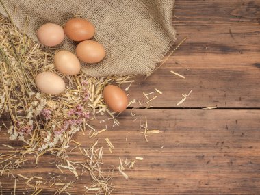 Kırsal çevre kahverengi tavuk yumurtası, çuval bezi ve saman eski ahşap plakalar arka plan üzerine bir parça ile arka plan. Üstten Görünüm. Paskalya kartları için yaratıcı arka plan