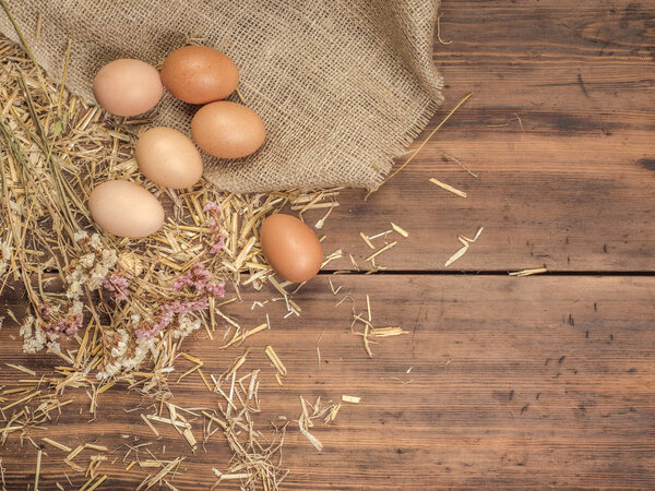 Деревенский экологический фон с коричневыми куриными яйцами, куском мешковины и соломой на фоне старых деревянных досок. Вид с вершины. Творческий фон для пасхальных открыток
