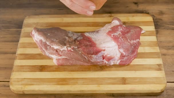 Een man kookt vlees op een cutting Board op de tafel van oude houten planken. Mannelijke handen strooi specerijen en politiewagens een stuk vlees. Koken van varkensvlees, rundvlees in de eigen keuken. Weergave van terug naar boven — Stockvideo