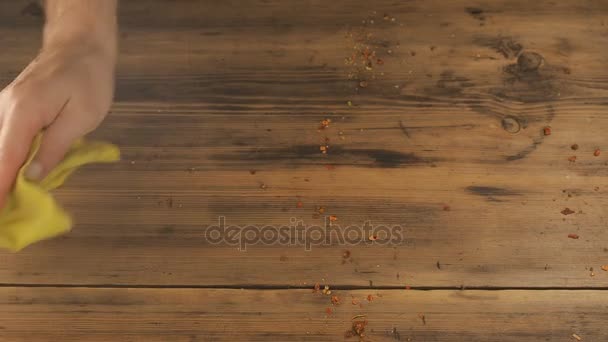 El hombre limpia la mesa de las viejas tablas marrones, tela amarilla. Mans mano elimina los restos de las especias de la mesa, elimina los escombros. La vista desde arriba — Vídeos de Stock