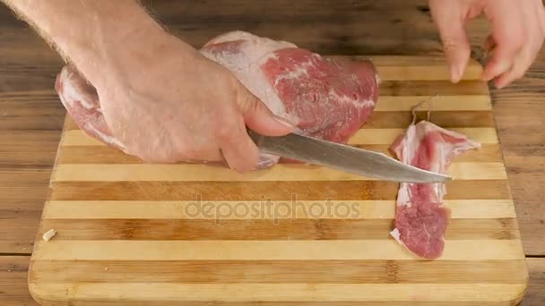 남자는 오래 된 나무 판자에서 테이블에 절단 보드에 고기 요리. 칼으로 남자 손 한 조각의 고기를 잘라. 요리 돼지고기, 쇠고기 집 부엌에서. 위쪽의 보기 — 비디오