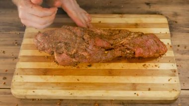 Bir adam eski ahşap plakalar tablosundan bir kesme tahtası üzerinde et yemek yapıyor. Erkek el baharat serpin ve bir et parçası çökmek. Domuz eti, yemek ev mutfak sığır. Görünümü en iyi