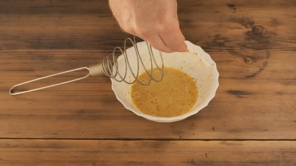 Mannen på hemmet köket lägger till salt i smeten från hönsägg. Vit skål med metall visp för att blanda på ett träbord från gamla styrelser. I smet av ägg och kryddor, sätta salt — Stockvideo