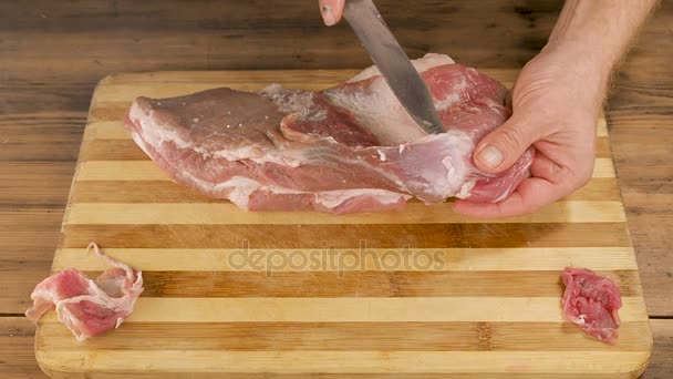 남자는 오래 된 나무 판자에서 테이블에 절단 보드에 고기 요리. 칼으로 남자 손 한 조각의 고기를 잘라. 요리 돼지고기, 쇠고기 집 부엌에서. 위쪽의 보기 — 비디오