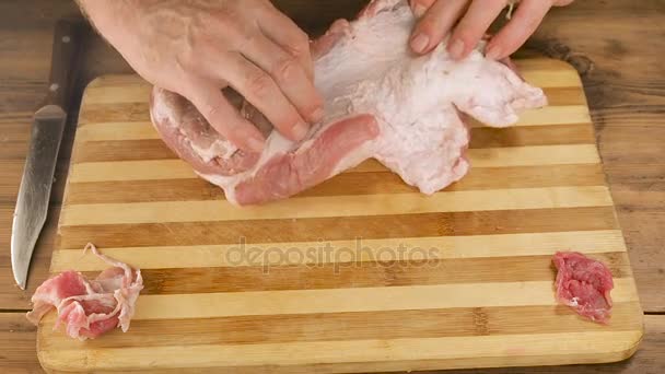 Un uomo cucina carne su un tagliere sul tavolo da vecchie assi di legno. Mano maschile con un coltello tagliare un pezzo di carne. Cucinare carne di maiale, manzo in cucina. Vista dall'alto — Video Stock