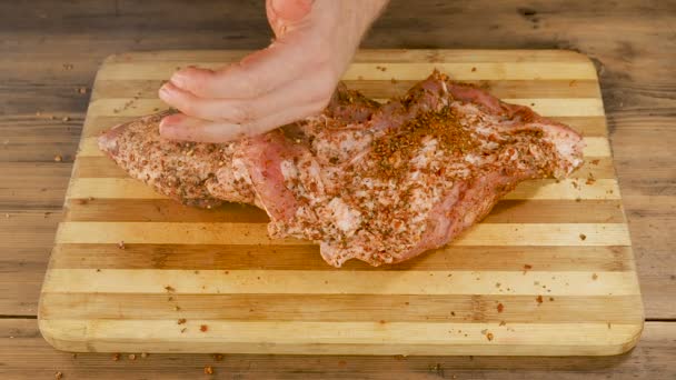 Чоловік готує м'ясо на обробній дошці на столі зі старих дерев'яних дощок. Чоловічі руки посипають спеціями і збивають шматочок м'яса. Готуємо свинину, яловичину на домашній кухні. Вид зверху — стокове відео