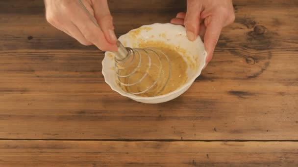 The man interfere the water in the batter. Cooking batter with eggs in the home kitchen. Mens hand prevented in a bowl egg, flour and water with whisk, on wooden background table from the old boards — Stock Video
