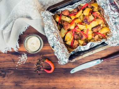 Et, sebze, biber ile fırında patates ile çeşitli kaba kumaş ve ahşap masa arka plan üzerine tuz. Fırın tepsisine, üstten görünüm folyo patates kızartma.