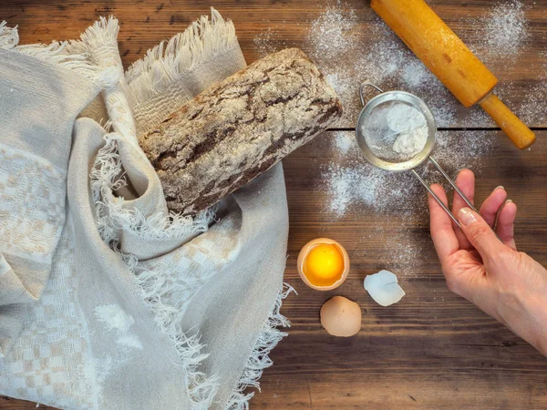 Kahverengi ekmek kırık kabuk ile eski ağacının bir arka plan üzerine kaba kumaştan bir bezle sarılmış ve un dağınık. Kadın el un sifts. Kompozisyon, rustik tarzda Üstten Görünüm