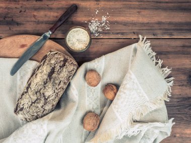 Bir kaba kumaş kumaştan kahverengi ekmek kırık kabuk ile sarılı. Tuz, ceviz, bıçak ve ahşap arka plan üzerine kumaş natürmort. Kompozisyon, rustik tarzda Üstten Görünüm