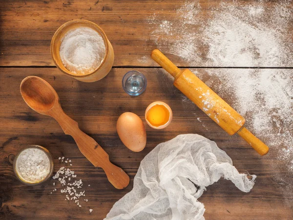 Spilled flour, salt, egg yolk, fabric, wooden spoon and rolling pin. Still life on the background of the old wooden table, top view in rustic style with kitchen utensils