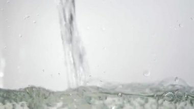 Su kabı, su akışı ve yükselen düzeyi dökülür. Su beyaz arka plan üzerinde yükselen kabarcıklar. Ateş su dökme. 60 fps Hd formatında vurdu.
