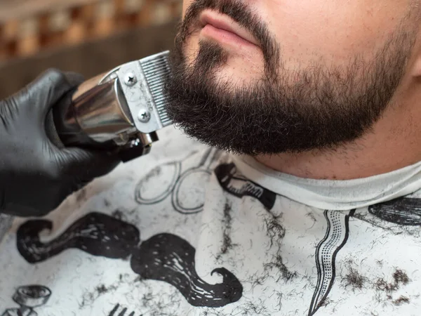 Homem na barbearia, vista de perto. Castor de corte estilista com clipper. Mãos em luvas de borracha preta. Foco suave seletivo. Fundo desfocado . — Fotografia de Stock