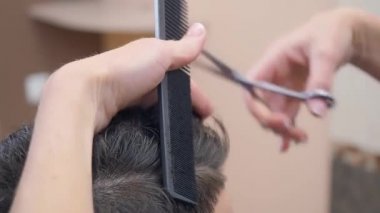 Ustalar müşterilerin saçlarını makas ve tarak ile kesiyor, yakın çekim. Kuaför salonunda kaydedilmiş. Seçici yumuşak odaklanma. Bulanık arkaplan.