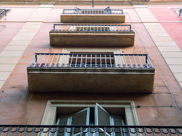 Barcelona, Spain - august 2019: pink building in city center, middle view. Balconies with black curved railing, bottom-up view. Selective soft focus. Blurred background