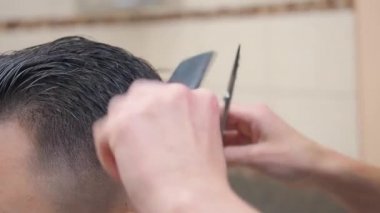 Makas ve tarakla saç kesen kuaförlerin yakın çekimleri. Kuaför salonunda kaydedilmiş. Berber dükkanında bir erkek. Seçici yumuşak odaklanma. Bulanık arkaplan.