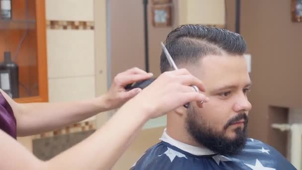 Hairstylist cutting mans hair with scissor and comb, close shot. Master at work in hairdressing saloon. Interior of barbershop. Selective soft focus. Blurred background. — Stock Video