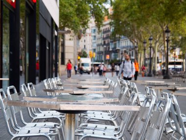 Barselona, İspanya - Ağustos 2019: Açık Cafe. Masalar ve sandalyeler caddede, orta manzara. Sokakta yürüyen insanlar. Yolda yeşil ağaçlar var. Araba sürüyor. Seçici yumuşak odaklanma. Bulanık arkaplan.