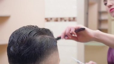 Müşterilerin saçını tarama ustası, yakın çekim. Saç kesme işlemi, berber dükkanında kaydedilmiş. Stilist iş başında. Seçici yumuşak odaklanma. Bulanık arkaplan.