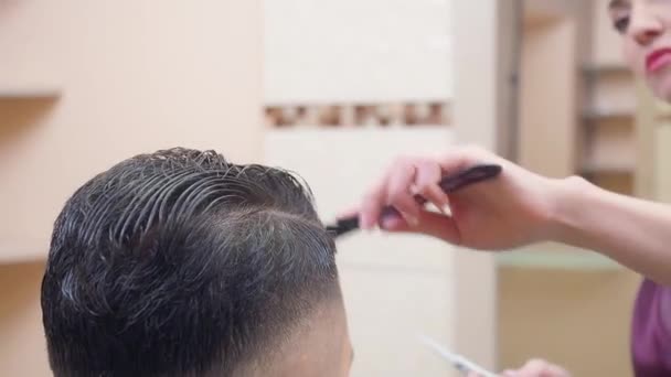 Mestre penteando clientes cabelo, tiro de perto. Processo de corte de cabelo, gravado na barbearia. Estilista no trabalho. Foco suave seletivo. Fundo desfocado . — Vídeo de Stock