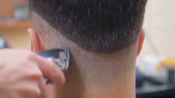 Hair cutting process, close shot. Stylist cutting males hair with clipper and comb. Mans nape close up. Recorded in barbershop. Selective soft focus. Blurred background. — Stock Video