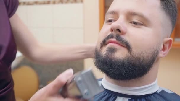 Maestro cortando barba machos con clipper y peine negro, tiro cerrado. Un hombre en la barbería. Los hombres miran de cerca. Enfoque suave selectivo. Fondo borroso . — Vídeos de Stock