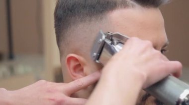 Stilist müşterilerin saçını kırpıcıyla kesiyor, yakın çekim. Kuaför salonunda yüksek lisans yapıyorum. Berber dükkanında bir erkek. Seçici yumuşak odaklanma. Bulanık arkaplan.