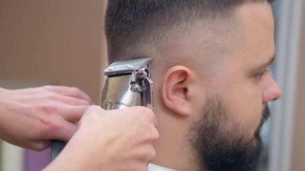 Мужчина в парикмахерской, с близкого расстояния. Стилист стрижет волосы на мужской затылке клиппером. Мастер в парикмахерской. Селективный мягкий фокус. Размытый фон . — стоковое видео