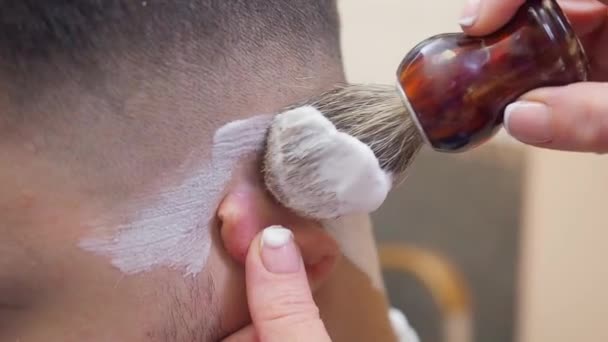 Barbier appliquer de la mousse à raser avec une brosse, plan rapproché. Homme dans le salon de coiffure. Coiffeur au travail. Mise au point sélective. Fond flou . — Video