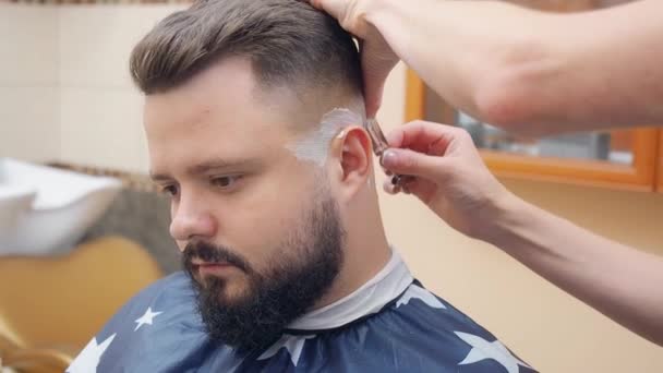 Barber shaving clients nape and temples with open razor, close shot. Male with beard in hairdressing saloon. Selective soft focus. Blurred background. — Stock Video