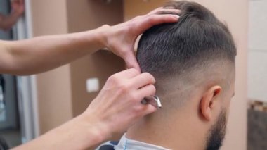Stilist erkek saçlarını jiletle kesiyor, yakın çekim. Berber dükkanındaki adam. Kuaför salonunun içi. Seçici yumuşak odaklanma. Bulanık arkaplan.