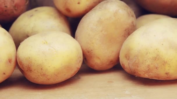 Panning shot alongside organic potato on wooden background. Dolly camera move, slowly sliding shot along potatoes is lying in bulk. Rustic vegetables from farmhouse field. — Stock Video